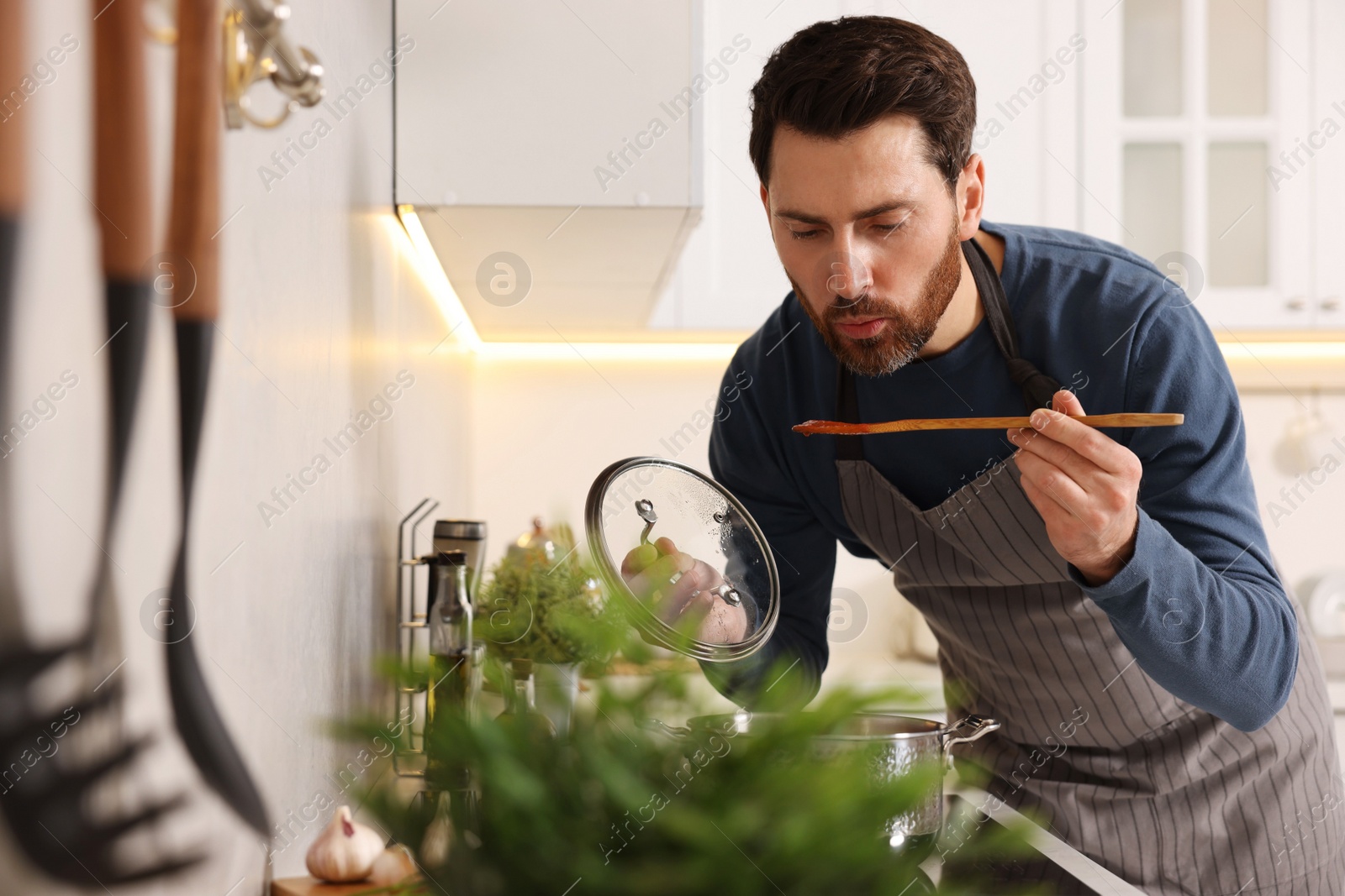 Photo of Man tasting delicious tomato soup in kitchen