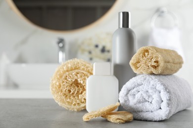 Photo of Natural loofah sponges, towel and cosmetic products on table in bathroom. Space for text