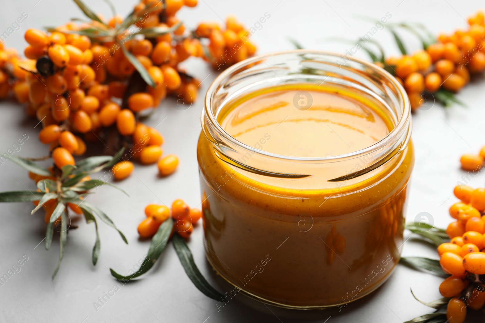 Photo of Delicious sea buckthorn jam and fresh berries on light grey table