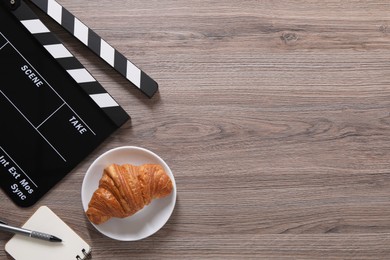 Photo of Movie clapper, croissant, notebook and pen on wooden table, flat lay. Space for text