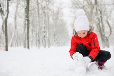 Photo of Cute little girl making snowballs outdoors on winter day, space for text