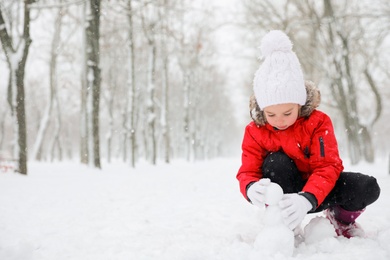 Cute little girl making snowballs outdoors on winter day, space for text