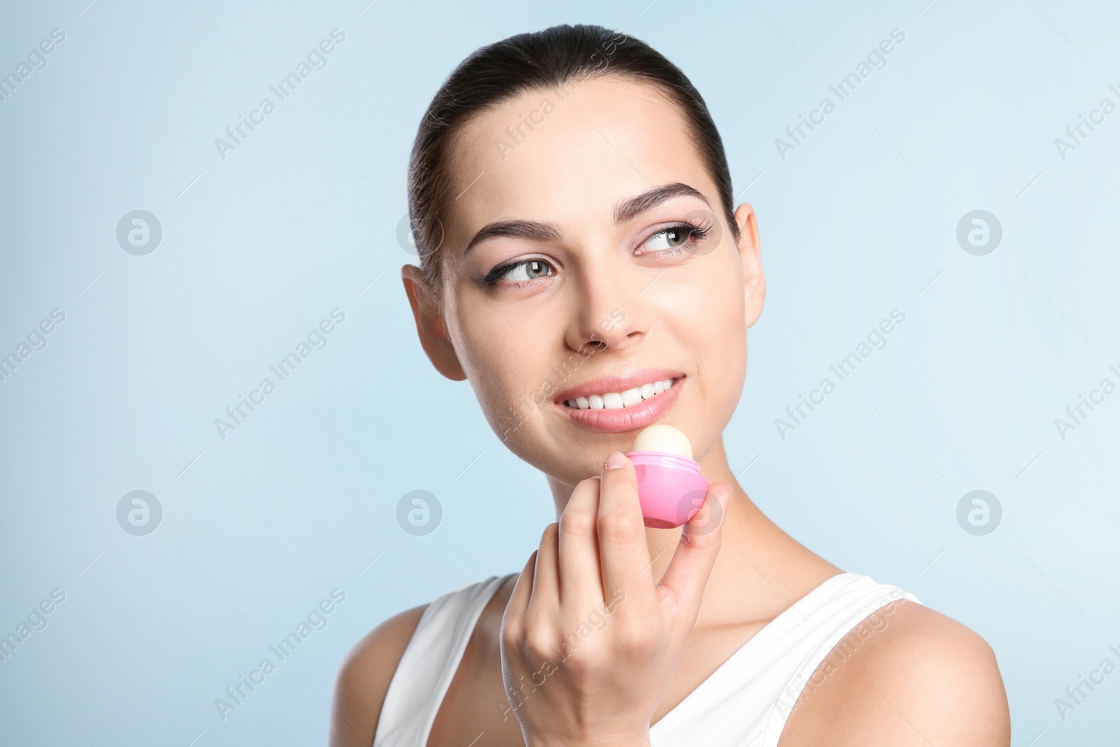 Photo of Young woman applying balm on her lips against color background