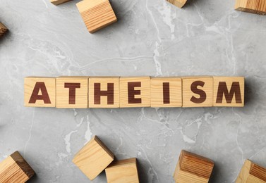 Word Atheism made of wooden cubes with letters on grey marble table, flat lay