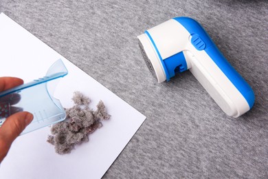 Photo of Woman holding fluff collector of fabric shaver and lint on light grey cloth, above view