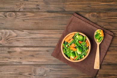 Bowl with different frozen vegetables on wooden table, top view