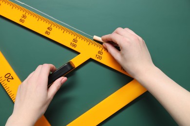 Photo of Woman drawing with chalk and triangle ruler on green board, closeup