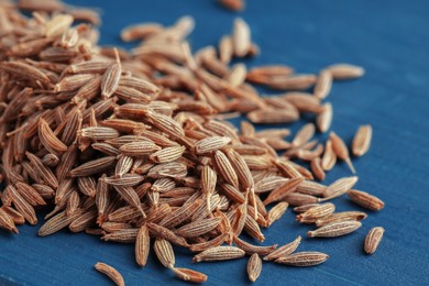 Photo of Pile of caraway seeds on blue wooden table, closeup