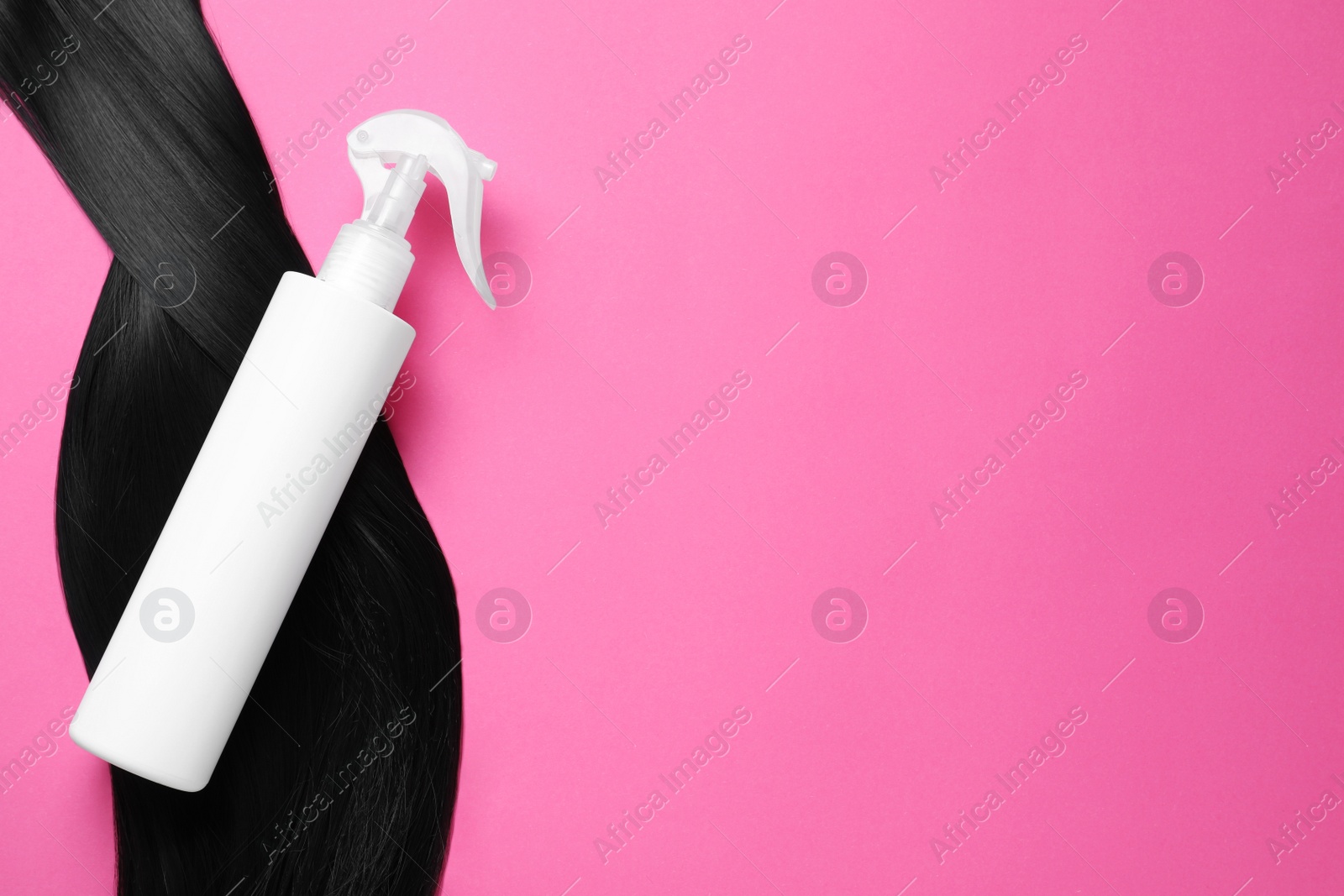 Photo of Spray bottle with thermal protection and lock of brunette hair on pink background, flat lay. Space for text