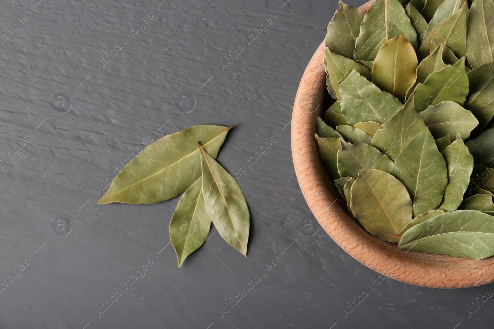 Photo of Aromatic bay leaves in wooden bowl on gray table, flat lay