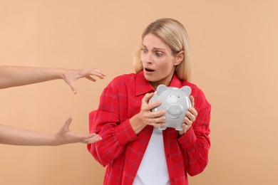 Photo of Scammer taking piggy bank from scared woman on beige background. Be careful - fraud