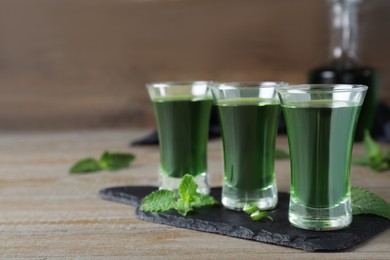 Photo of Delicious mint liqueur with green leaves on wooden table, closeup. Space for text