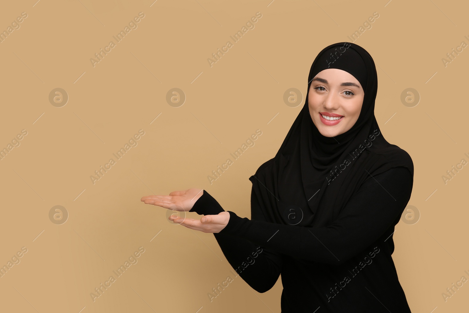 Photo of Muslim woman in hijab pointing at something on beige background