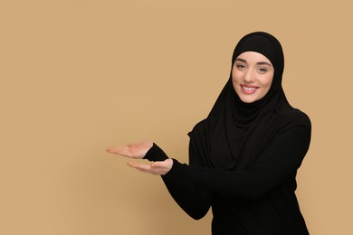 Muslim woman in hijab pointing at something on beige background