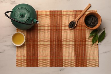 Photo of Flat lay composition with bamboo mat, dry tea leaves and teapot on white marble table, top view. Space for text