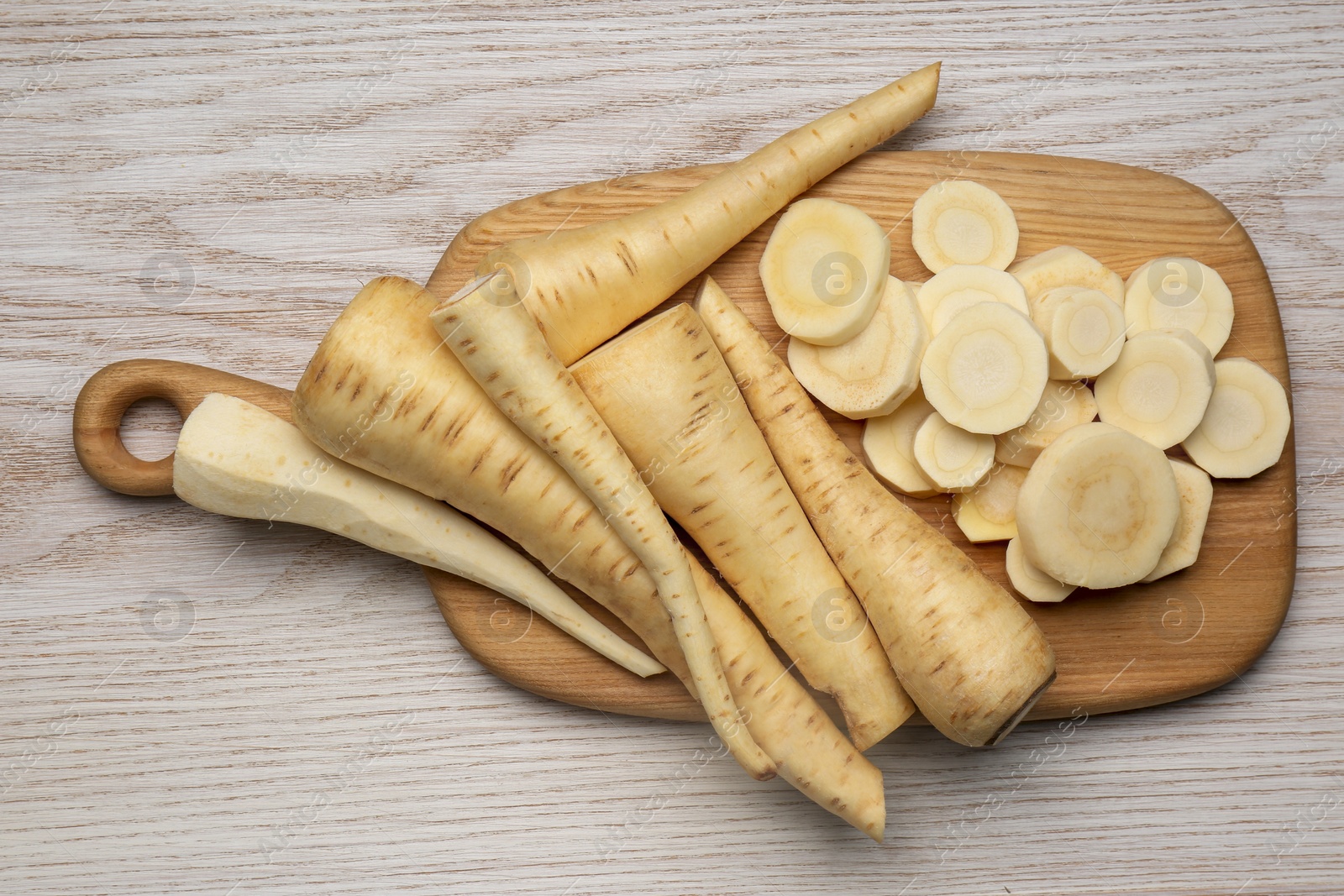 Photo of Whole and cut fresh ripe parsnips on white wooden table, top view