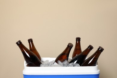Photo of Blue plastic cool box with ice cubes and beer on beige background, closeup. Space for text