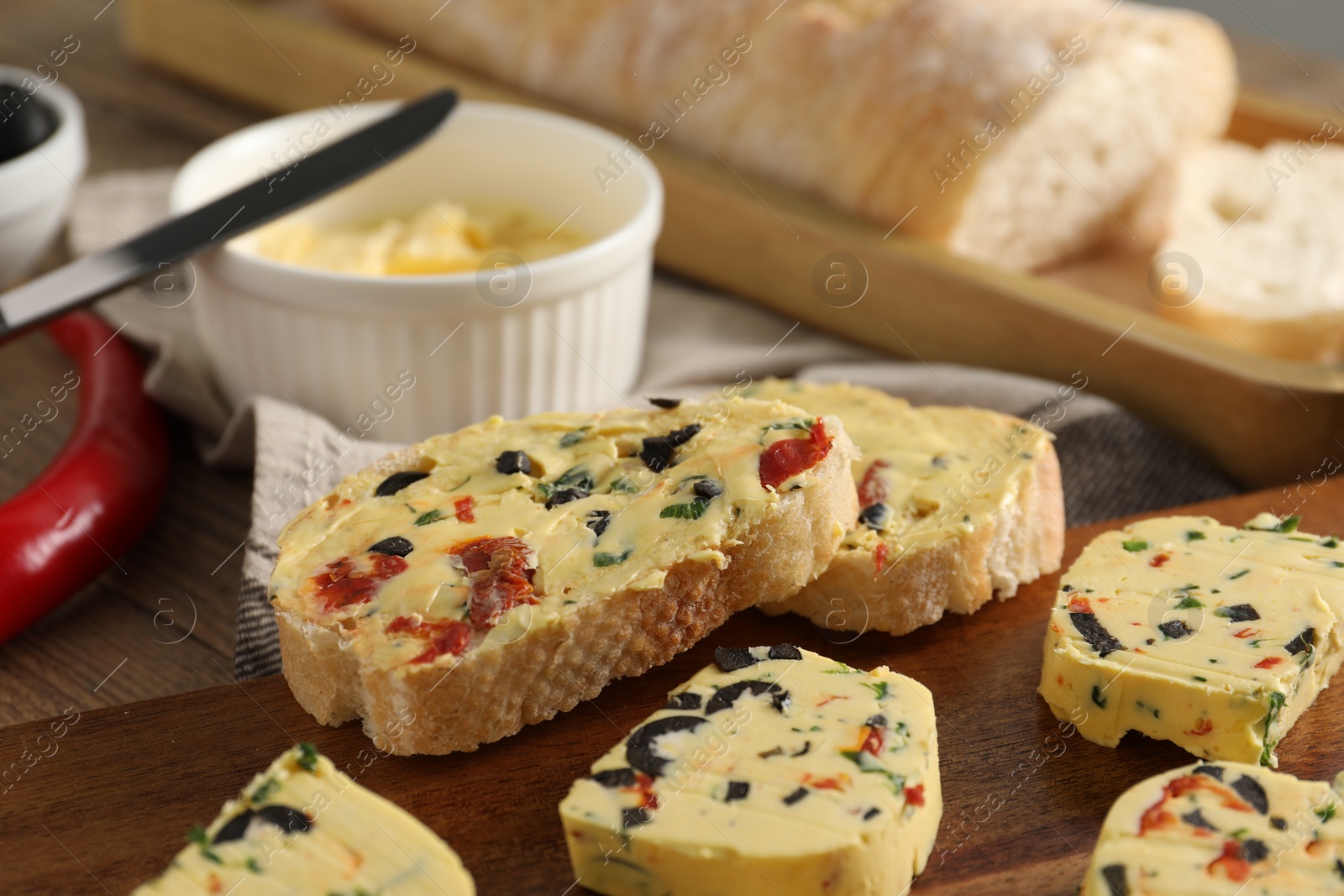 Photo of Tasty butter with olives, chili pepper, parsley and bread on wooden table, closeup