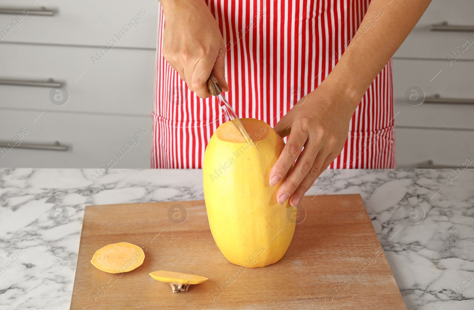 Photo of Woman cutting ripe spaghetti squash on table in kitchen, closeup