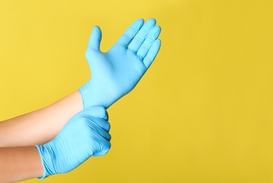 Person putting on blue latex gloves against yellow background, closeup. Space for text
