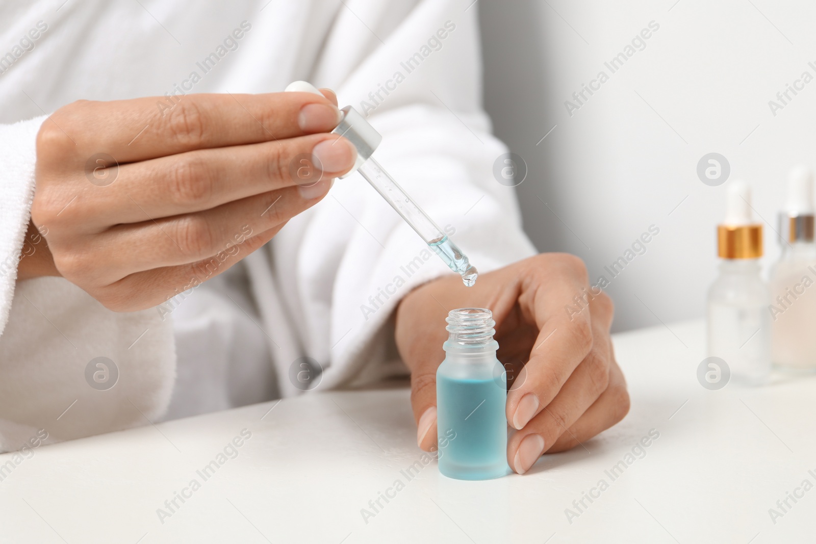 Photo of Woman with cosmetic serum at white table, closeup