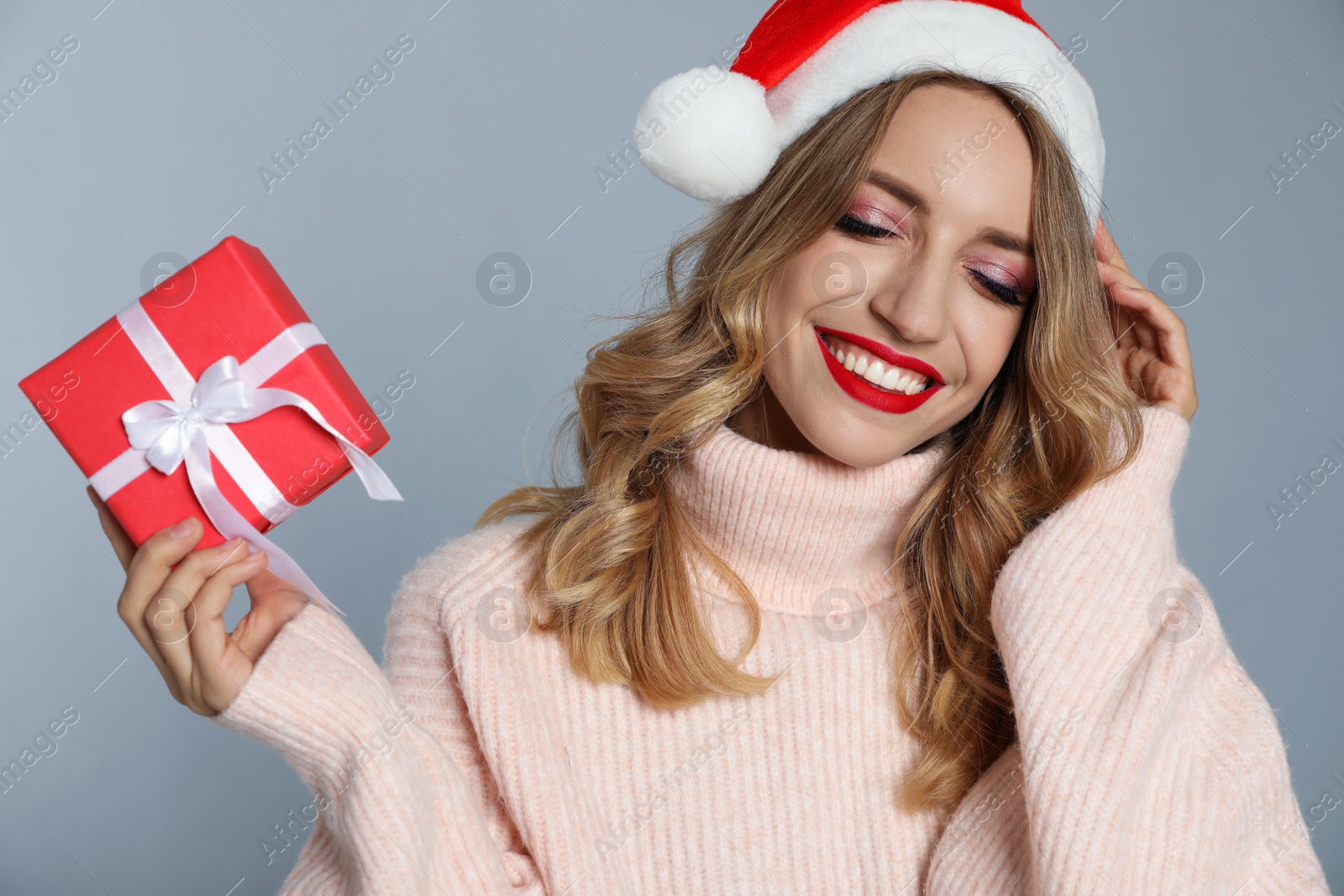 Photo of Happy young woman wearing Santa hat with Christmas gift on grey background