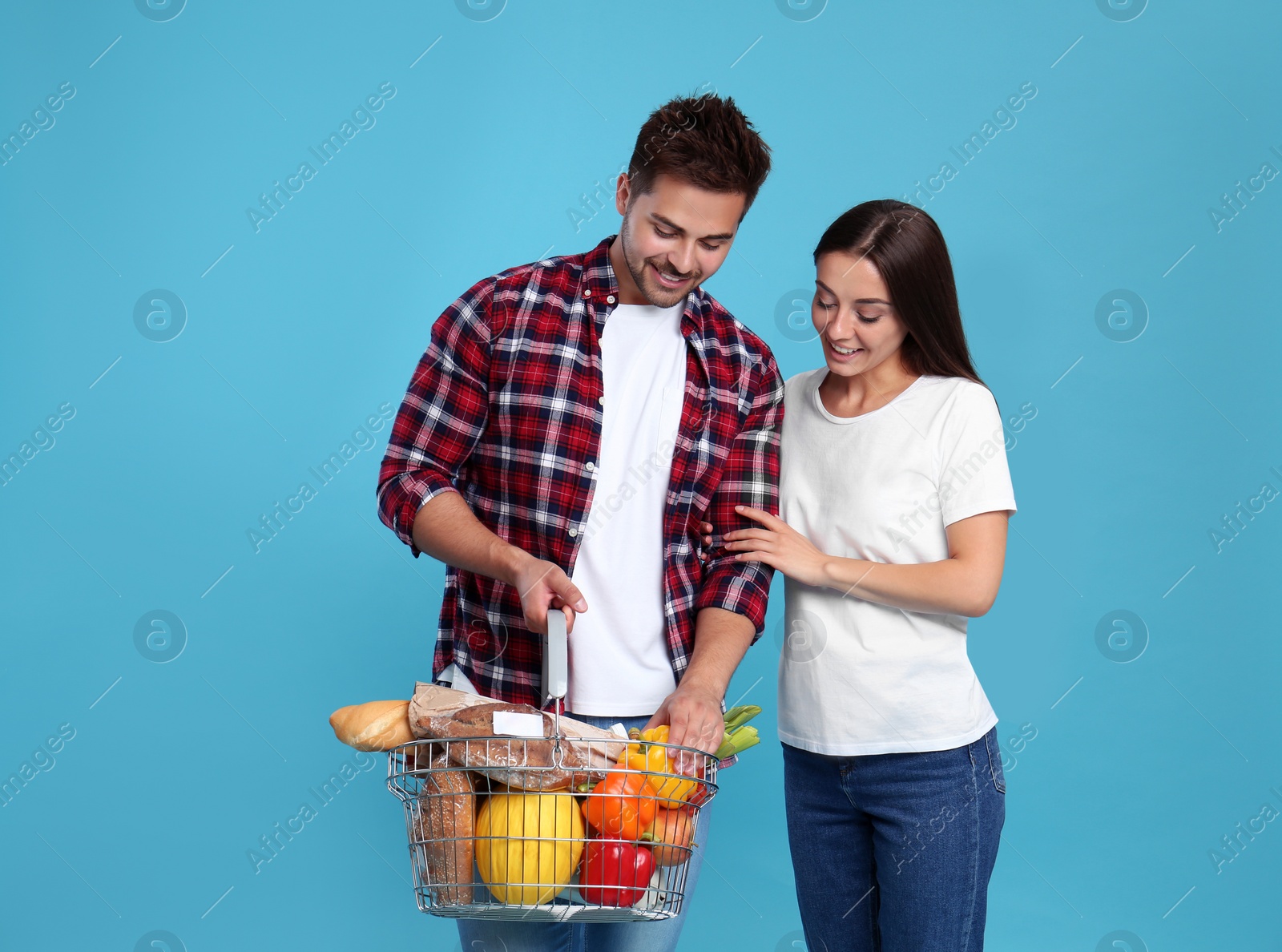 Photo of Young couple with shopping basket full of products on blue background