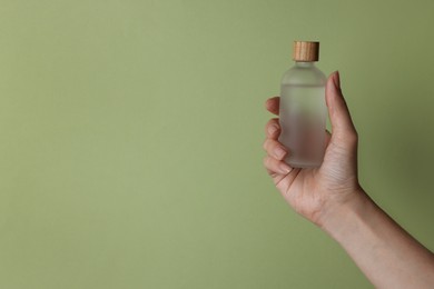 Woman holding bottle of cosmetic product on pale olive background, closeup. Space for text