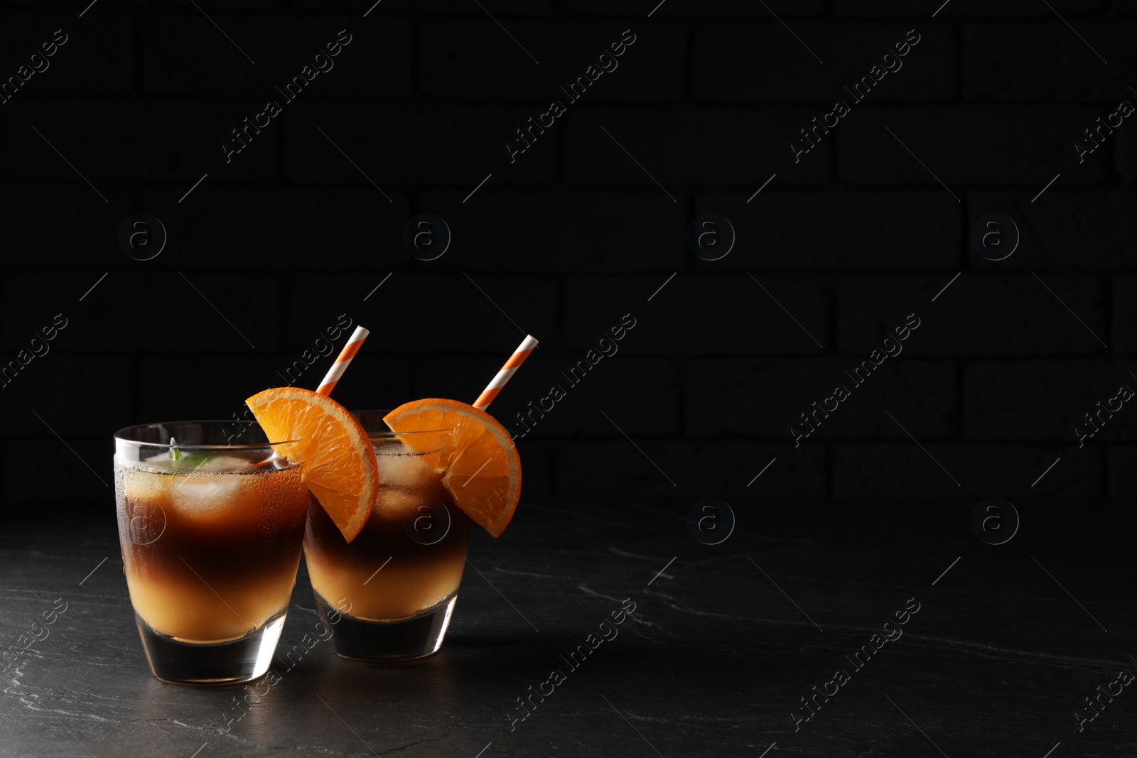 Photo of Tasty refreshing drink with coffee and orange juice on grey table against dark background, space for text