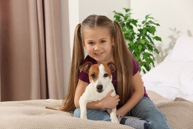 Photo of Cute girl hugging her dog on bed indoors. Adorable pet