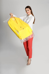 Young woman holding hanger with jacket on light grey background. Dry-cleaning service