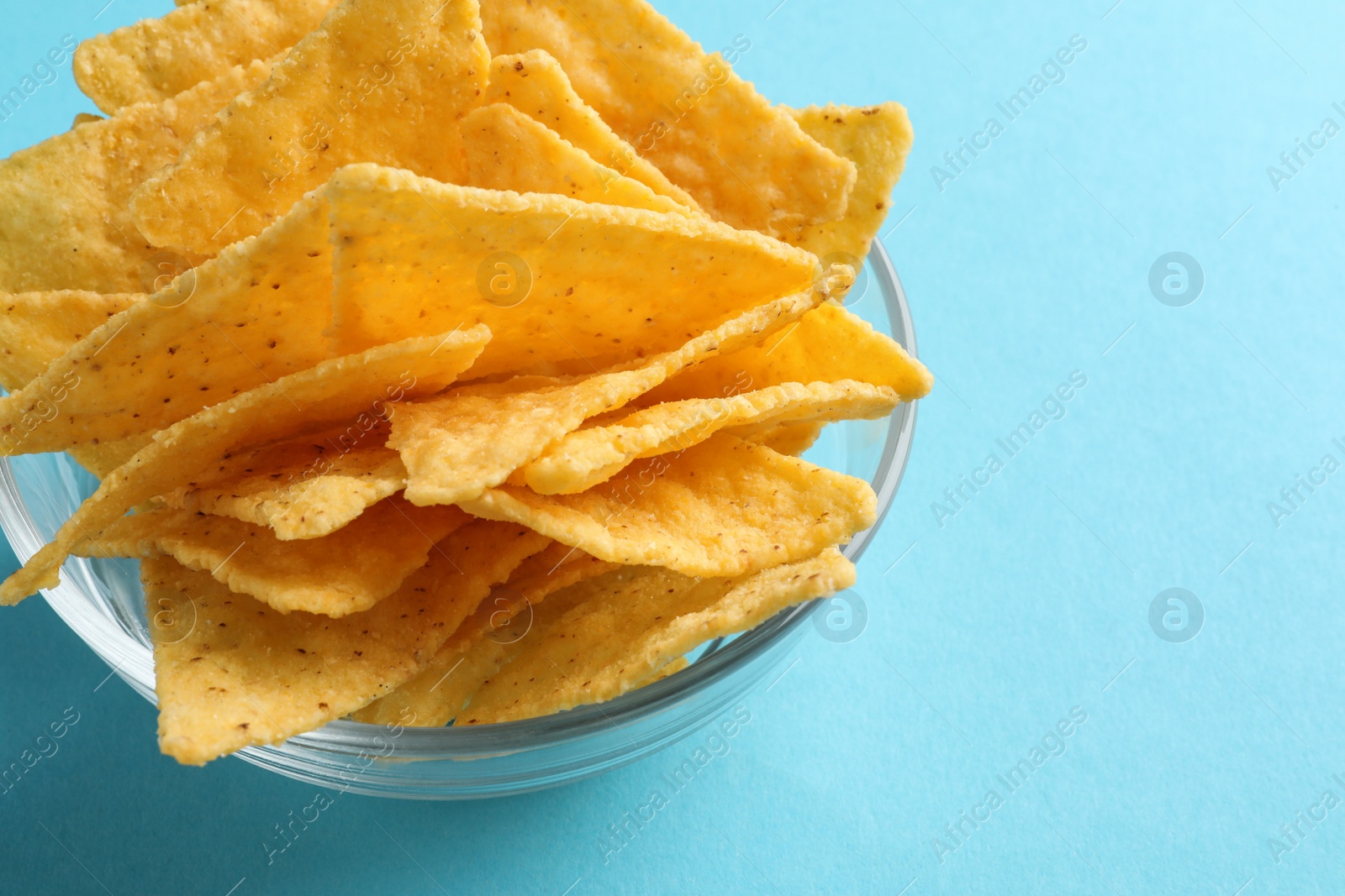 Photo of Tortilla chips (nachos) in glass bowl on light blue background, closeup