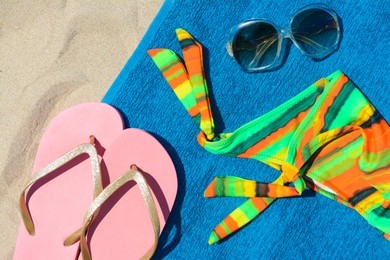 Soft blue beach towel with flip flops, sunglasses and colorful bikini bottom, flat lay