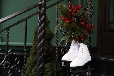 Photo of Pair of ice skates and Christmas wreath hanging on metal railing outdoors
