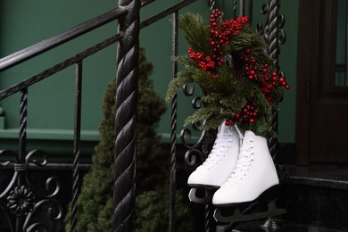 Pair of ice skates and Christmas wreath hanging on metal railing outdoors