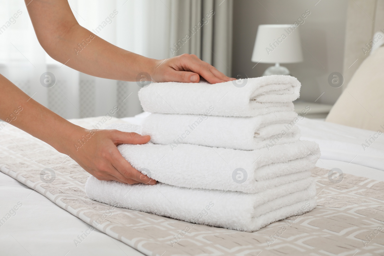 Photo of Woman putting fresh towels on bed in room, closeup