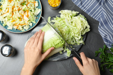Photo of Woman cutting chinese cabbage on grey table, top view