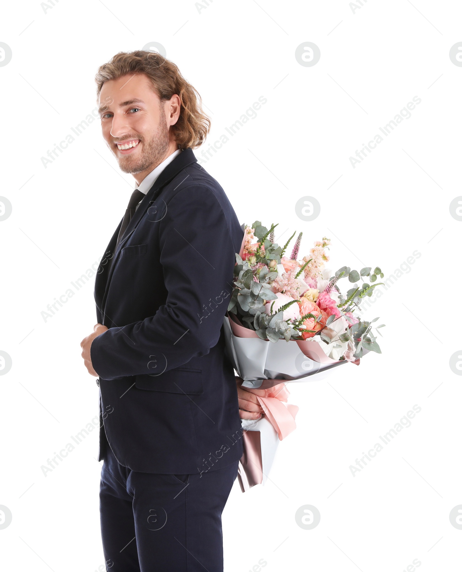 Photo of Young handsome man in stylish suit hiding beautiful flower bouquet behind his back on white background