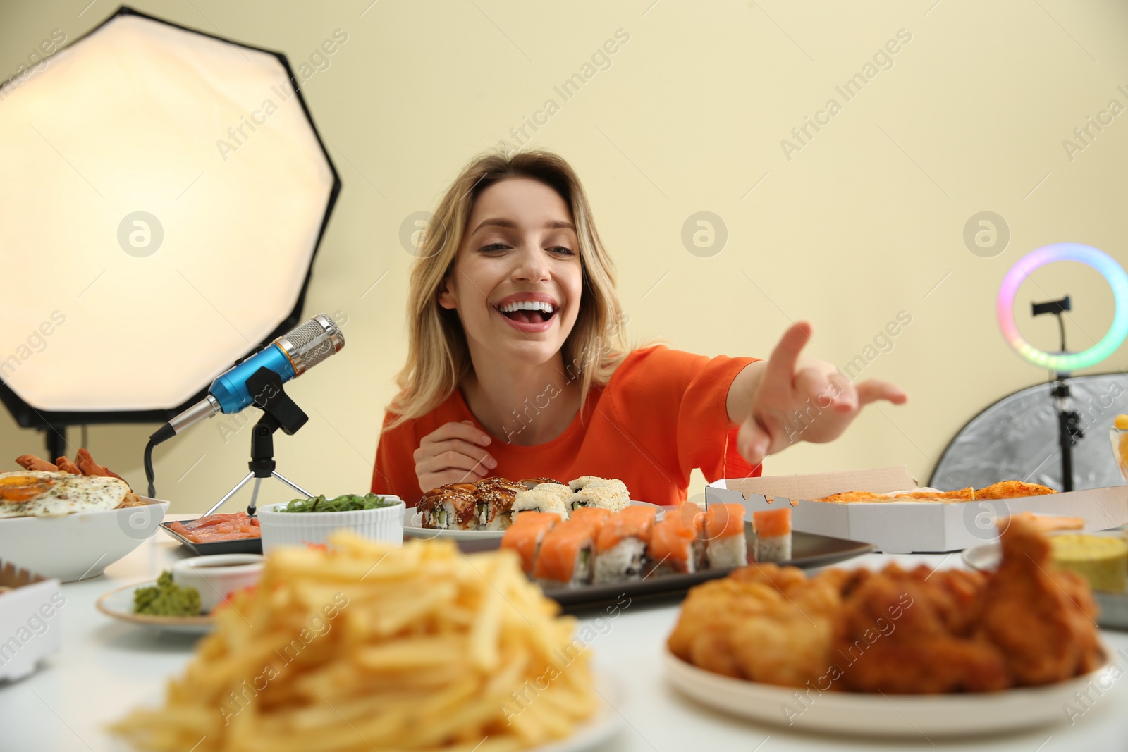 Photo of Food blogger eating in front of microphone at table against light background. Mukbang vlog