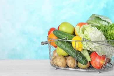 Photo of Basket with ripe fruits and vegetables on white table against blue background. Space for text
