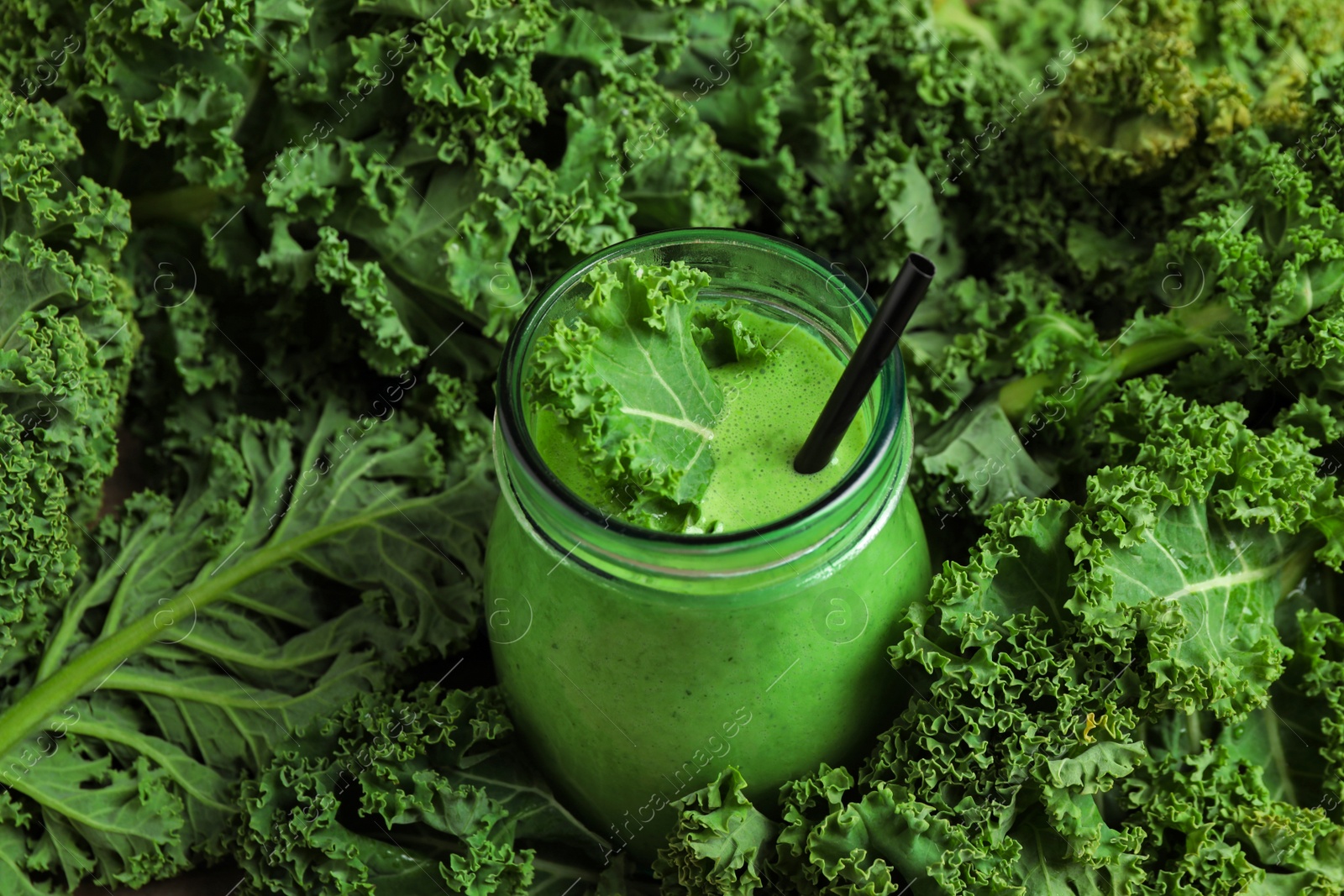 Photo of Tasty fresh kale smoothie in green leaves, closeup