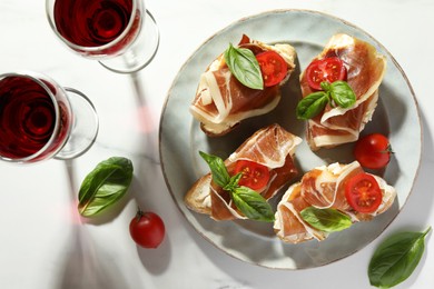 Tasty sandwiches with cured ham, basil and tomatoes on white marble table, flat lay