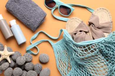 String bag and different beach accessories on pale orange background, flat lay