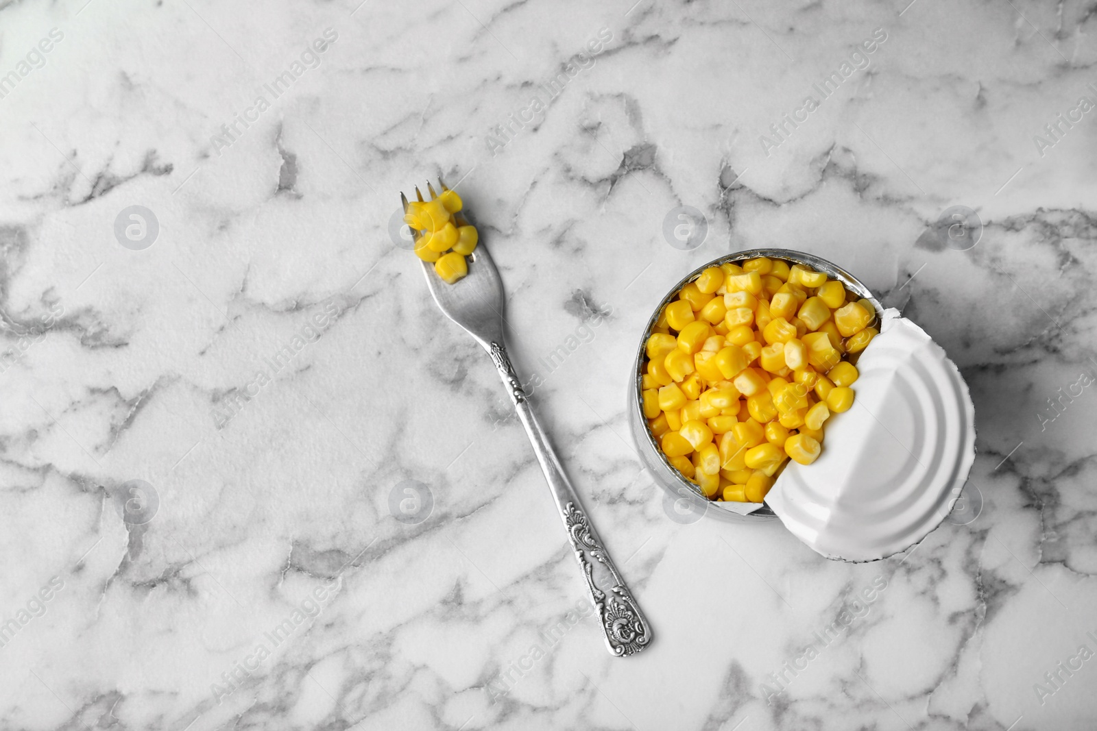 Photo of Tin can and fork with conserved corn on marble background, top view