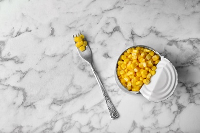 Photo of Tin can and fork with conserved corn on marble background, top view