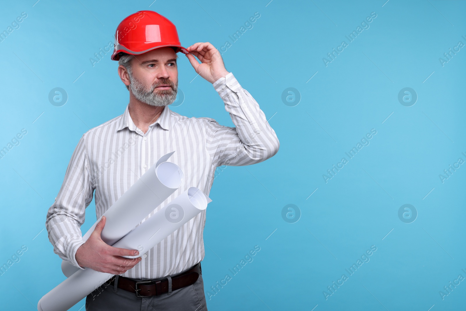 Photo of Architect in hard hat holding drafts on light blue background. Space for text