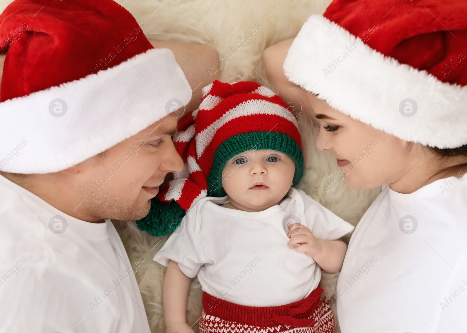 Photo of Happy couple with baby in Christmas hats on fuzzy rug, top view