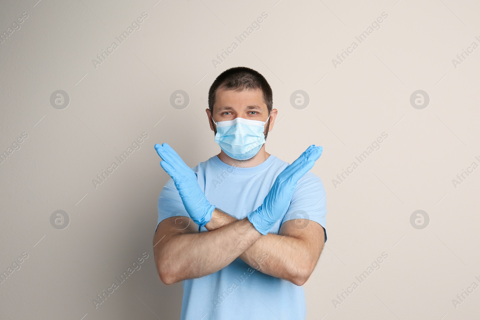 Photo of Man in protective mask showing stop gesture on beige background. Prevent spreading of COVID‑19