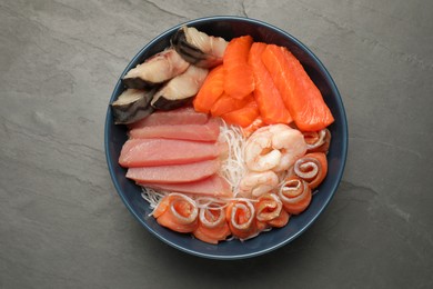 Photo of Delicious mackerel, salmon, shrimps and tuna served with funchosa on grey table, top view. Tasty sashimi dish