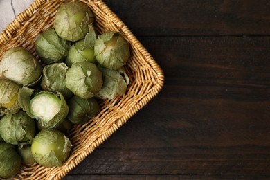 Photo of Fresh green tomatillos with husk in wicker basket on wooden table, top view. Space for text